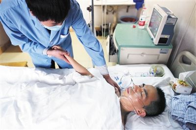 昨日，术后的万金强躺在病床上，护工在给他按摩手臂。新京报记者薛珺摄